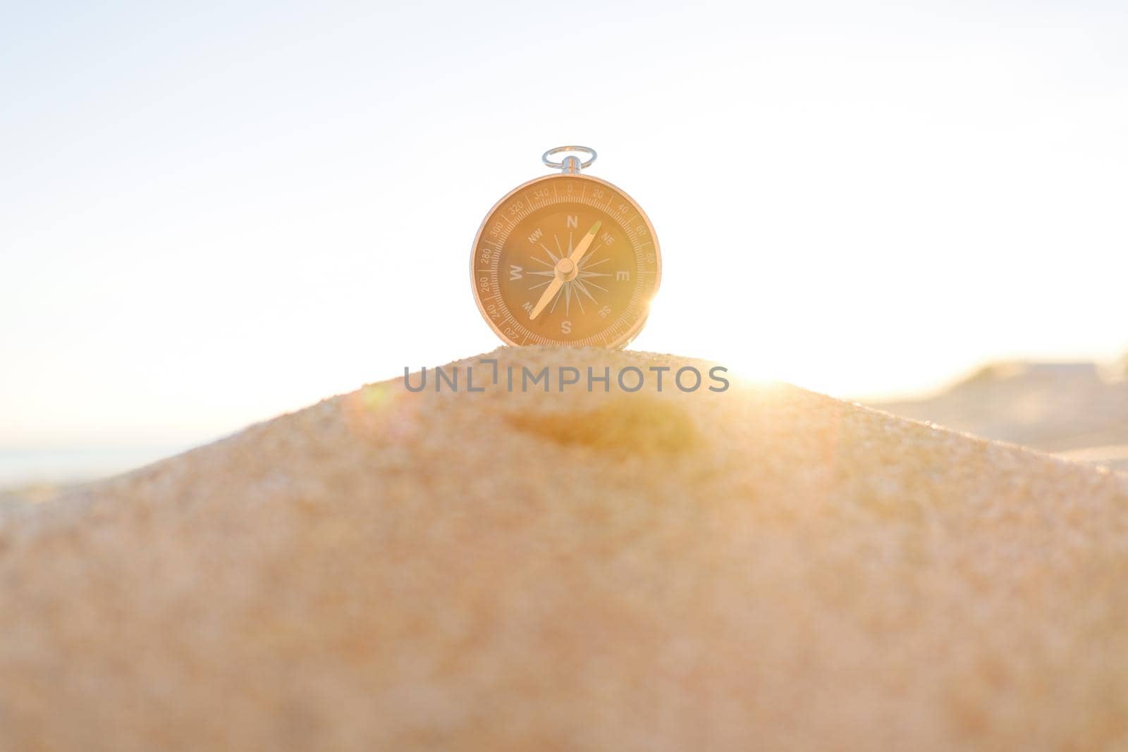 Magnetic compass on sand on sunny summer day, concept of travel and vacations.