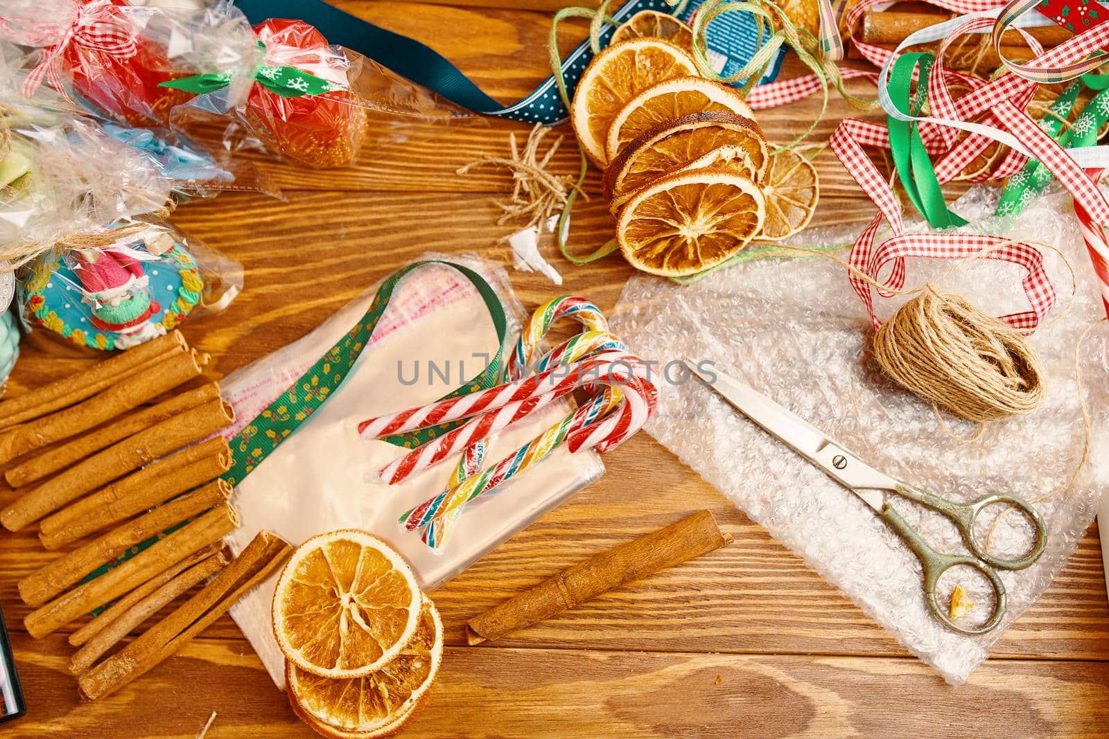 Wooden table with Christmas decor. Cinnamon sticks, candy canes, souvenirs, slices of dried oranges, colorful ribbons, scissors and wrapper. New Year's composition. Gift packaging.