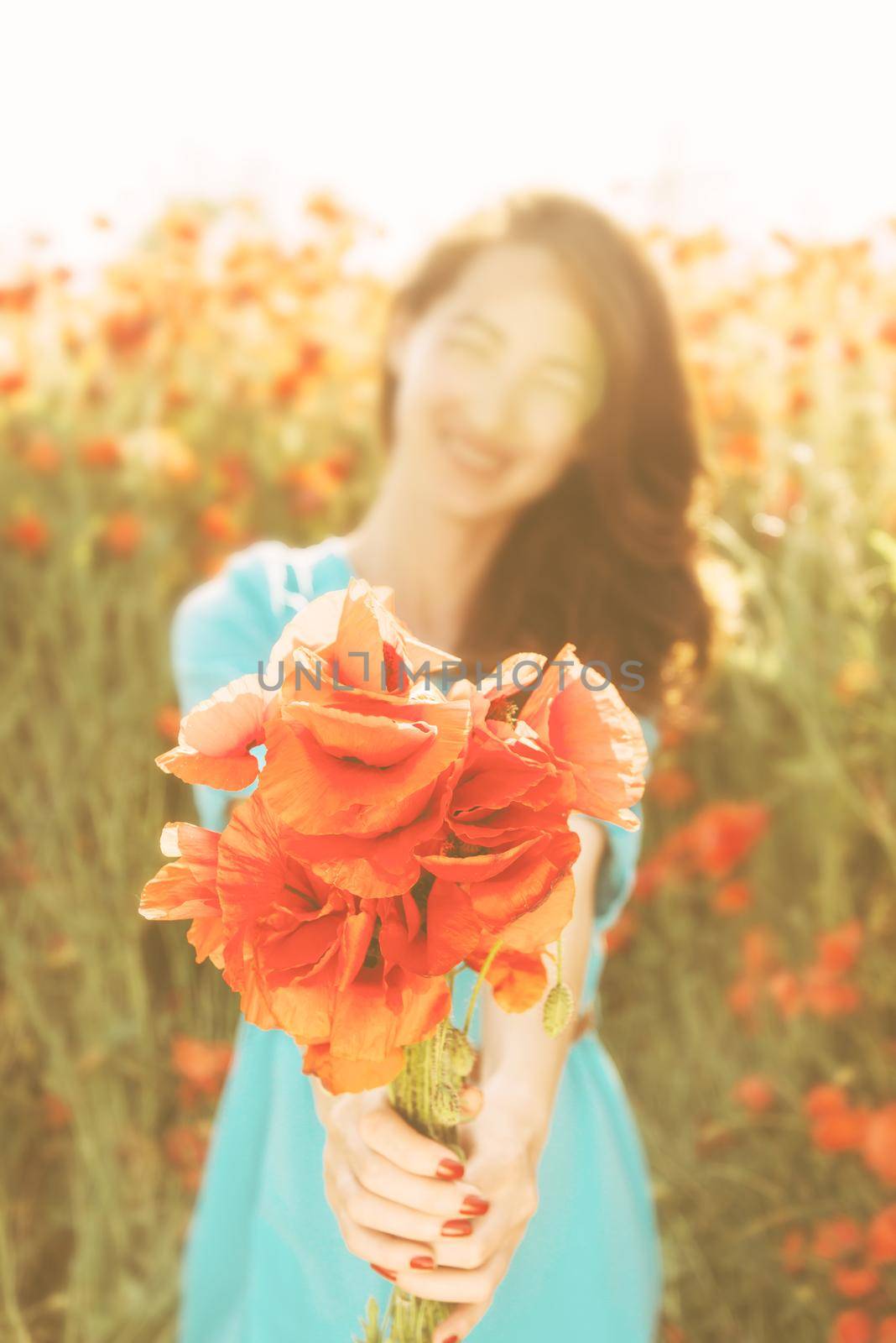 Smiling beautiful young woman giving a bouquet of red poppies in summer, focus on flowers.