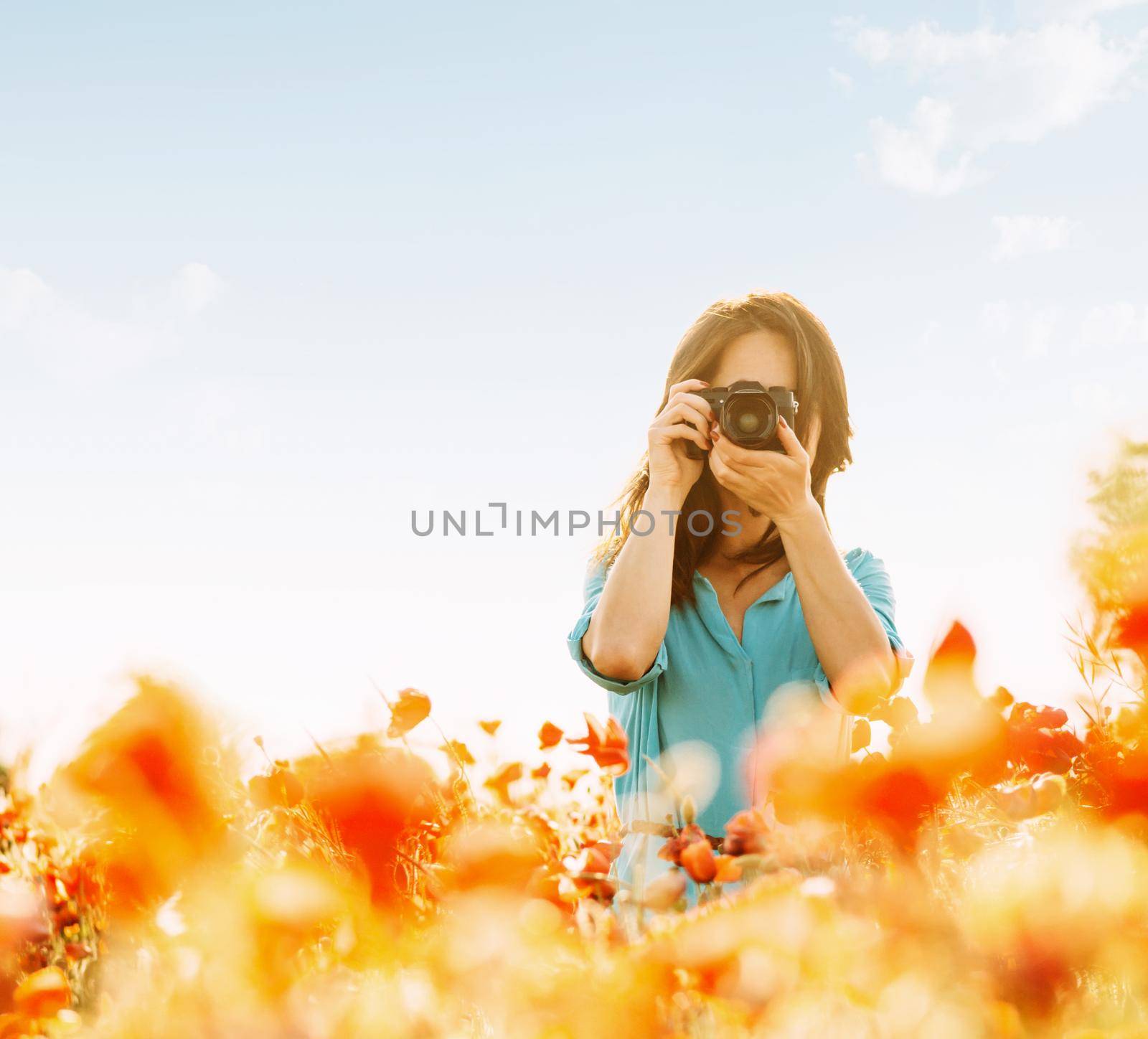 Girl photographing with a camera in flower meadow in summer outdoor.