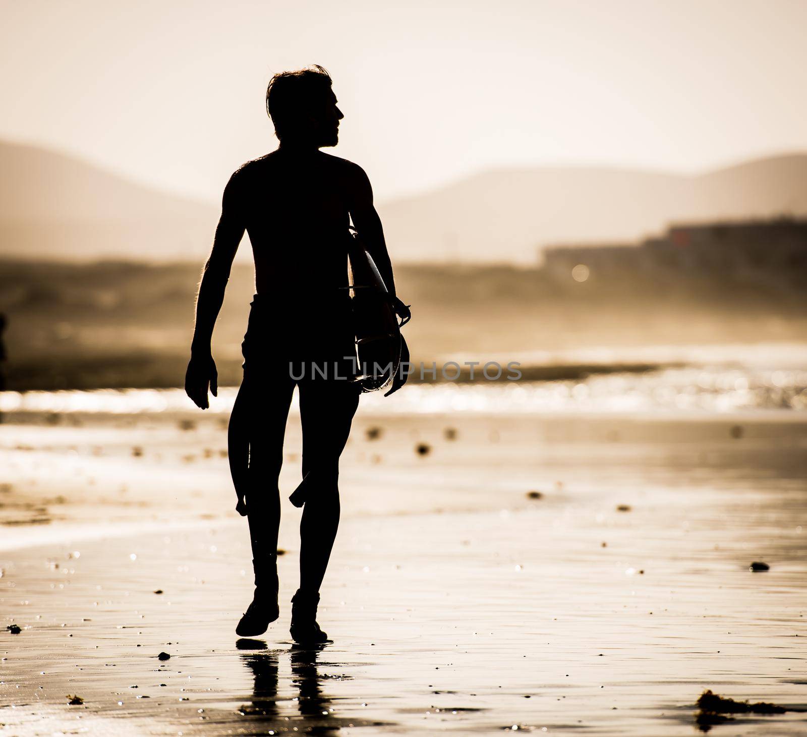Silhouette of the man walking on the beach with the surfboard