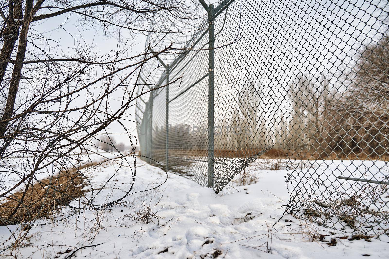 Escape from prison or closed institution for mentally ill. Hole in border fence with barbed wire. Unauthorized entry is prohibited. Maximum security detention facility. Illegal trespassing. Winter.