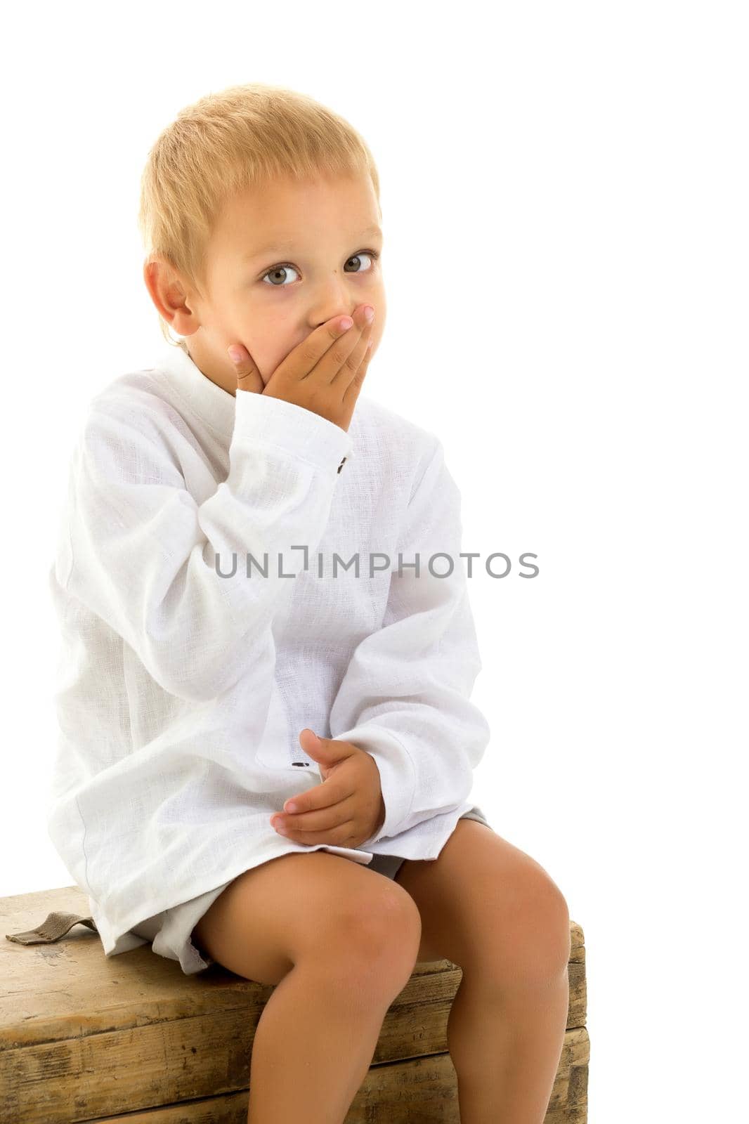 A cute little boy is sitting on an old chest. Isolated over white background.