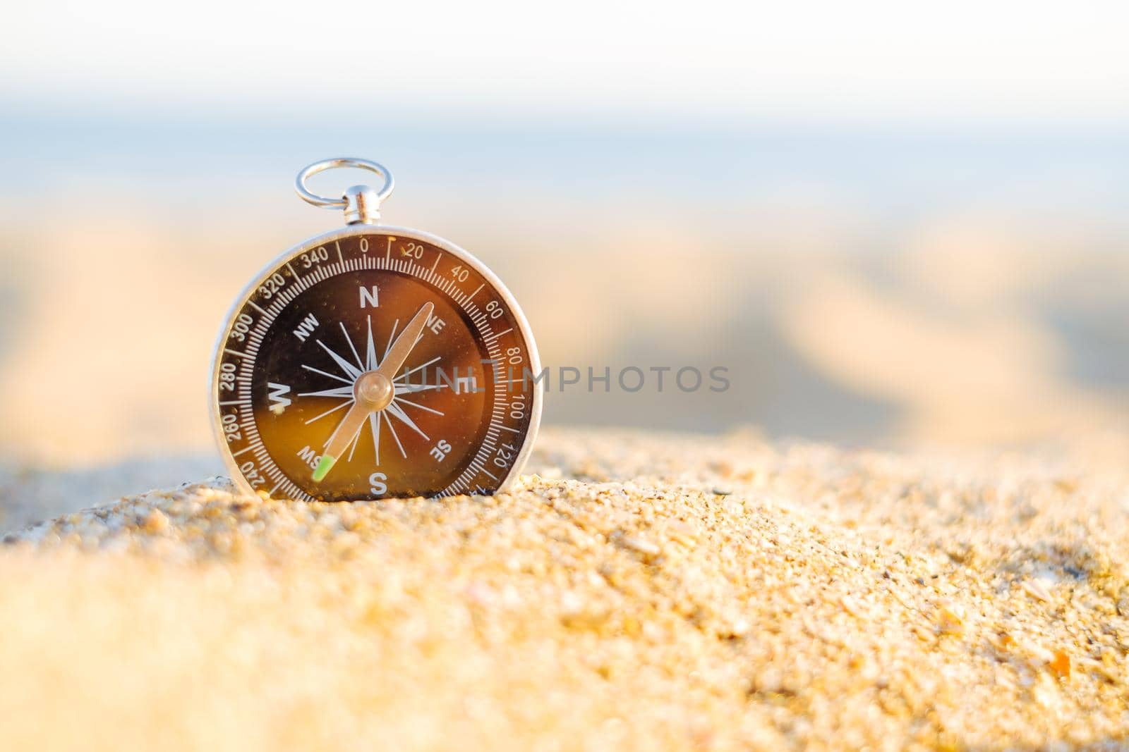 Travel compass on sand on sunny day outdoor.