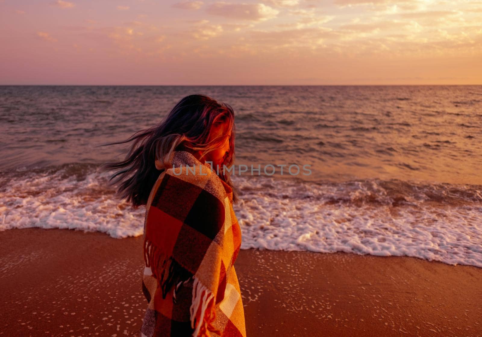 Young woman walking on sand coast near the sea at sunset.