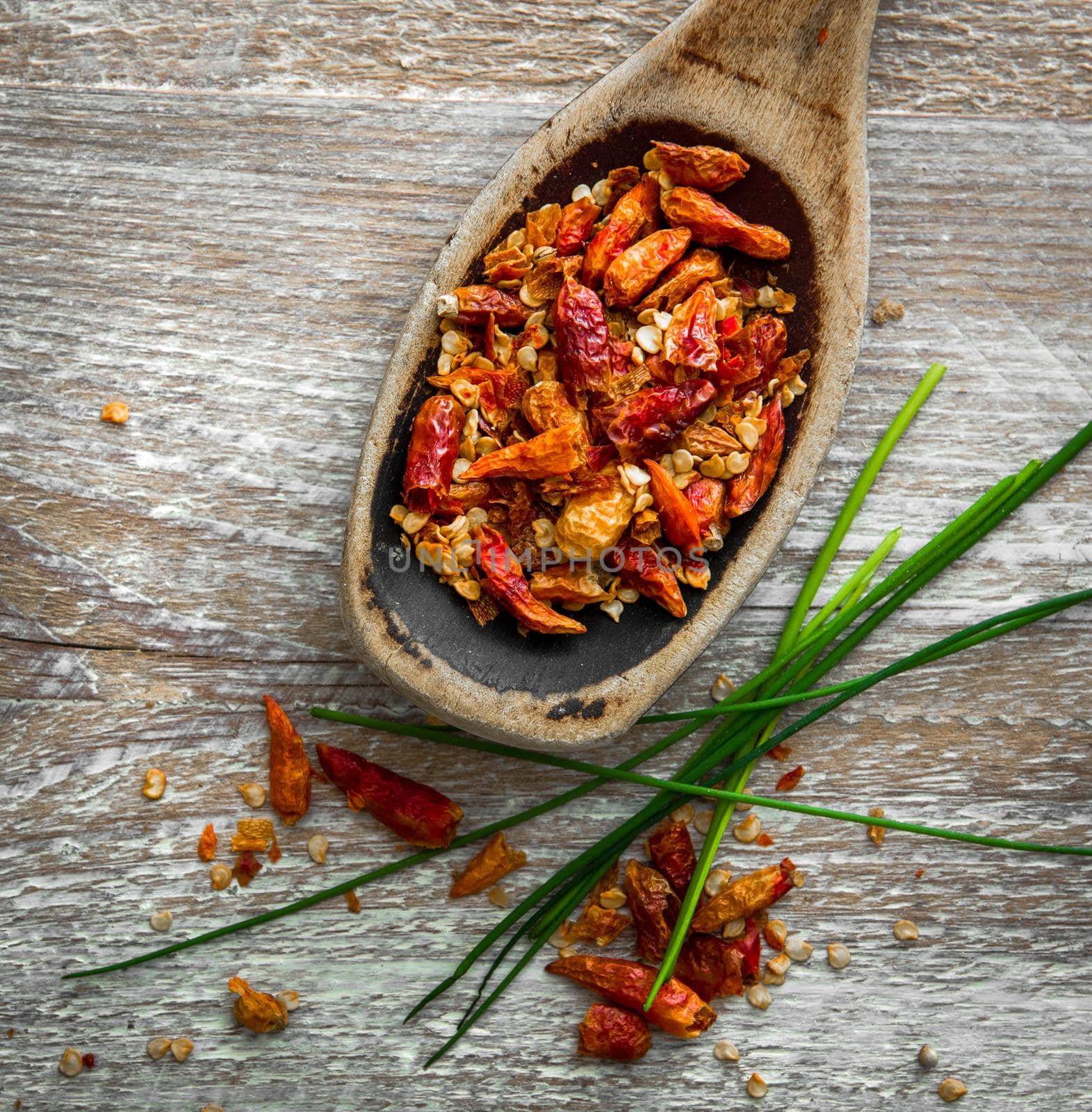Dried chili pepper in a wooden spoon on a textured background