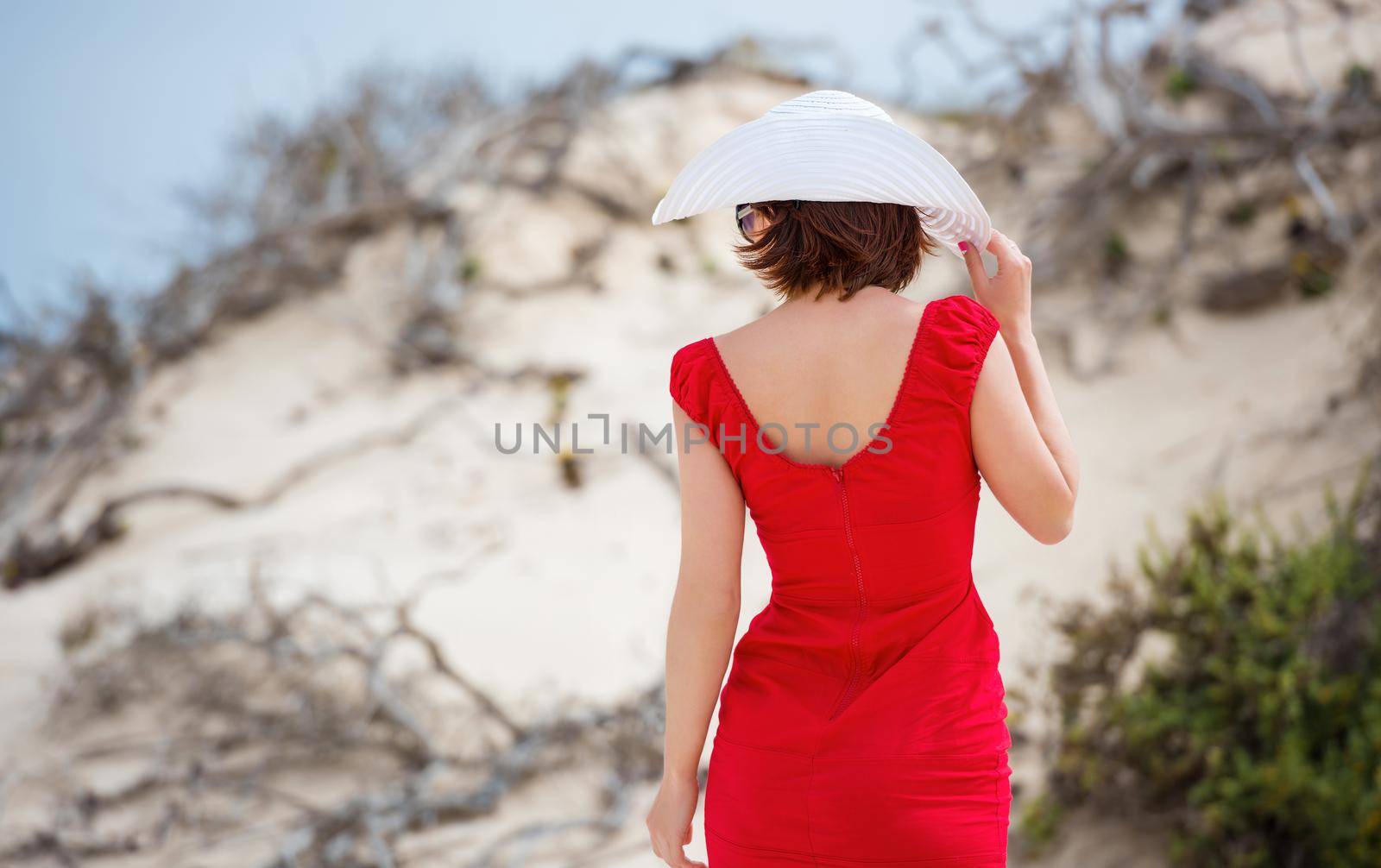 beautiful young woman in evening red dress and white hat on a background of a sand desert