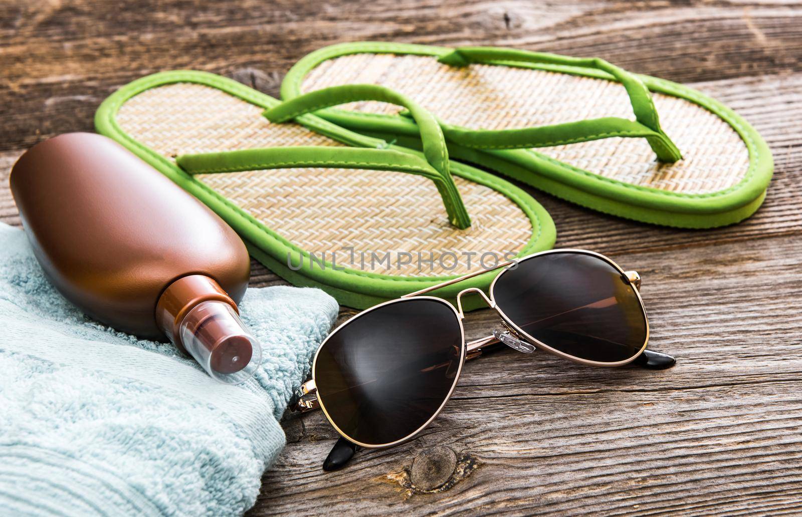 Beach accessories. Summer shoes and towel with sunglasses and suntan lotion on a wooden background