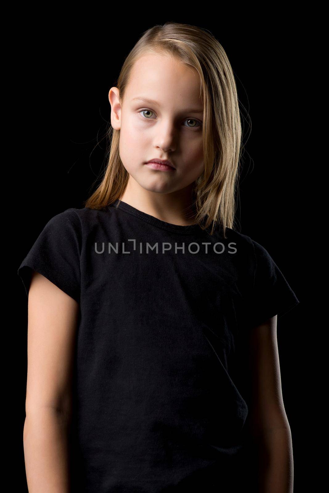 Close-up portrait of a beautiful blonde teenage girl in a black t-shirt on a black background. by kolesnikov_studio