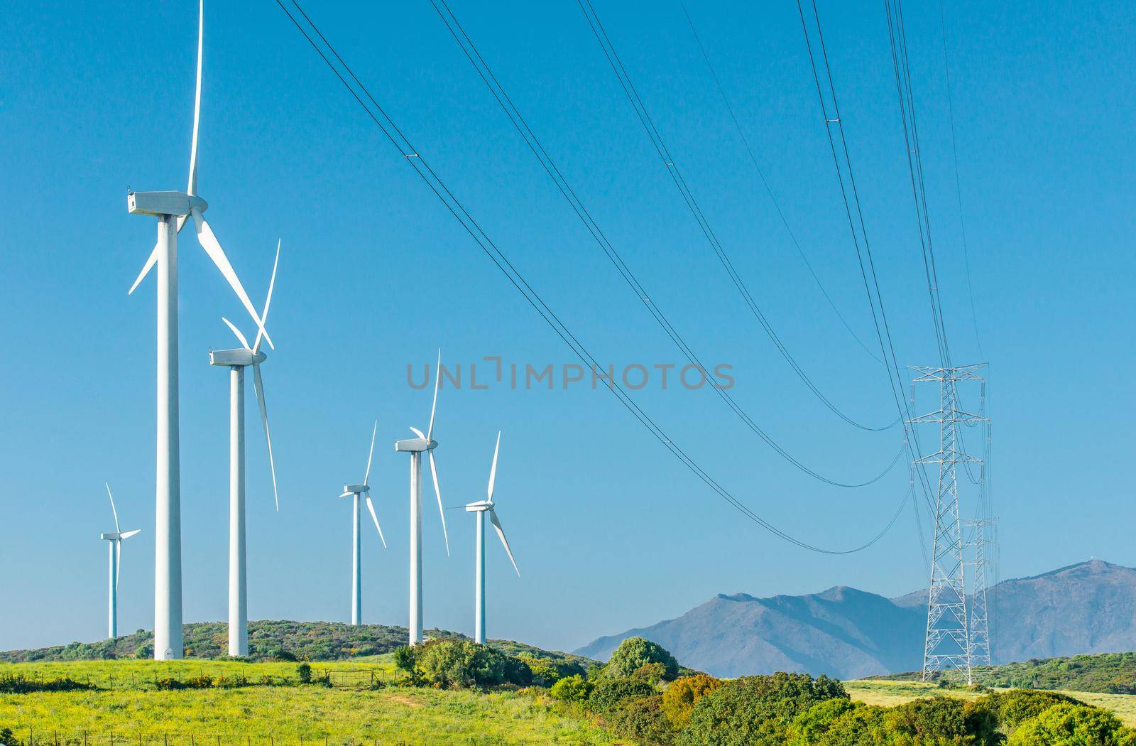 wind generator and high-voltage lines in a field on with blue sky and mountains on background