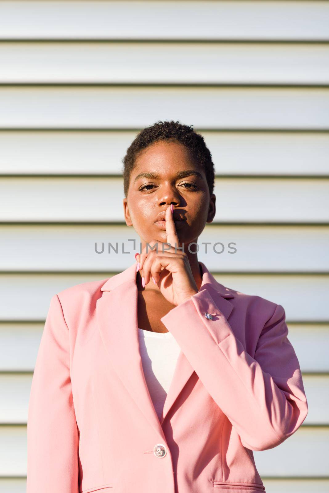 Black businesswoman doing silence gesture. African american female wearing suit with pink jacket with sunset light.