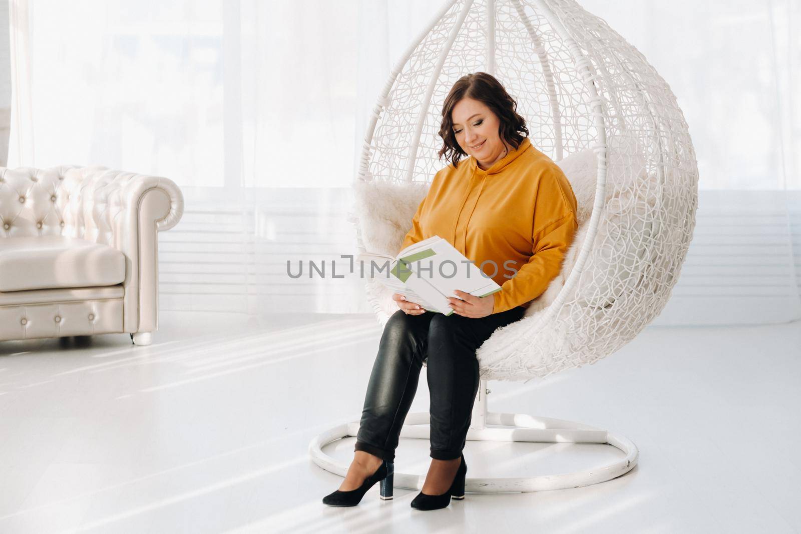 a woman in an orange hoodie sits in an unusual chair with a book in her hands.