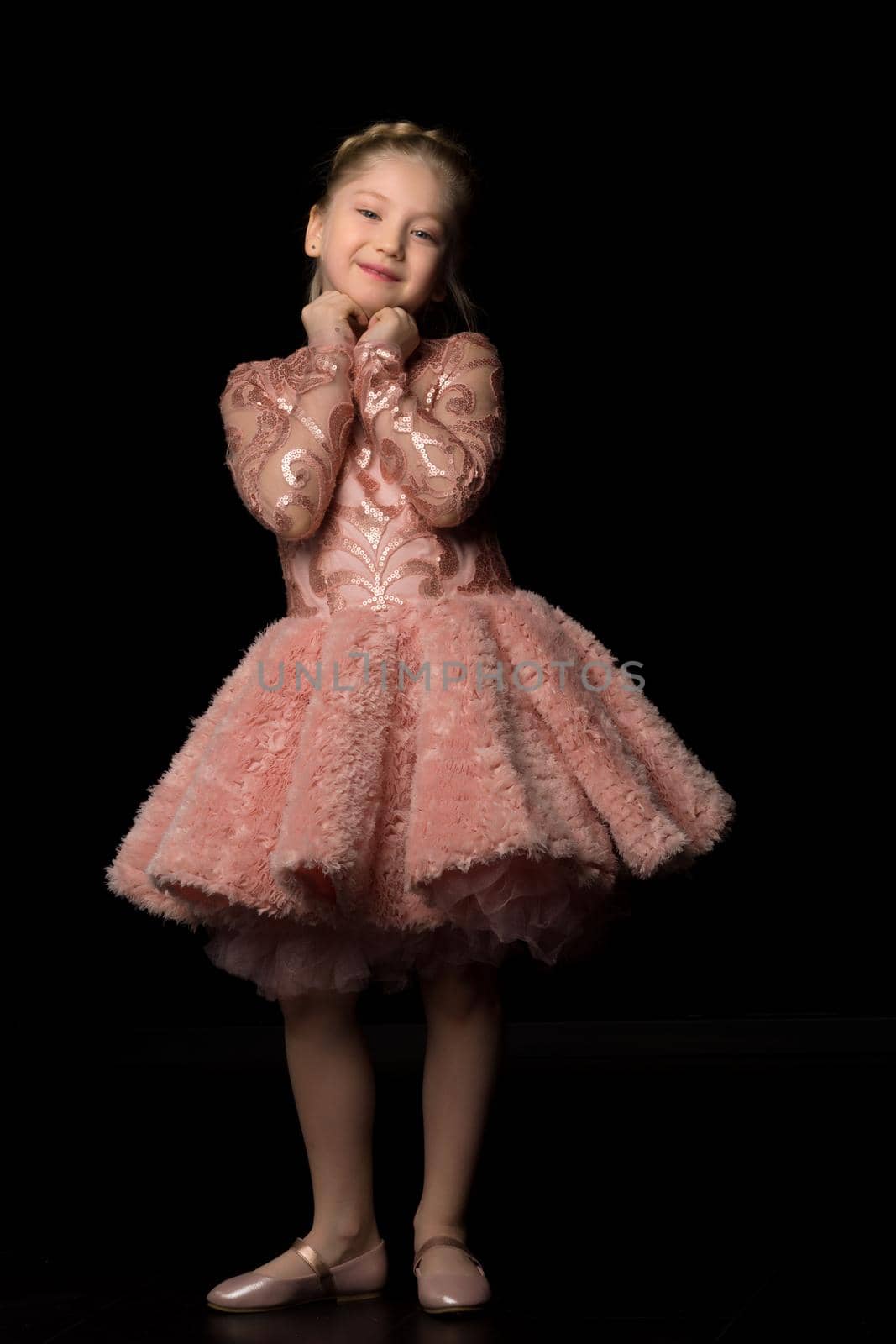 A charming little girl folded her hands around her face. The concept of beauty and fashion, children's emotions. Isolated on a black background.