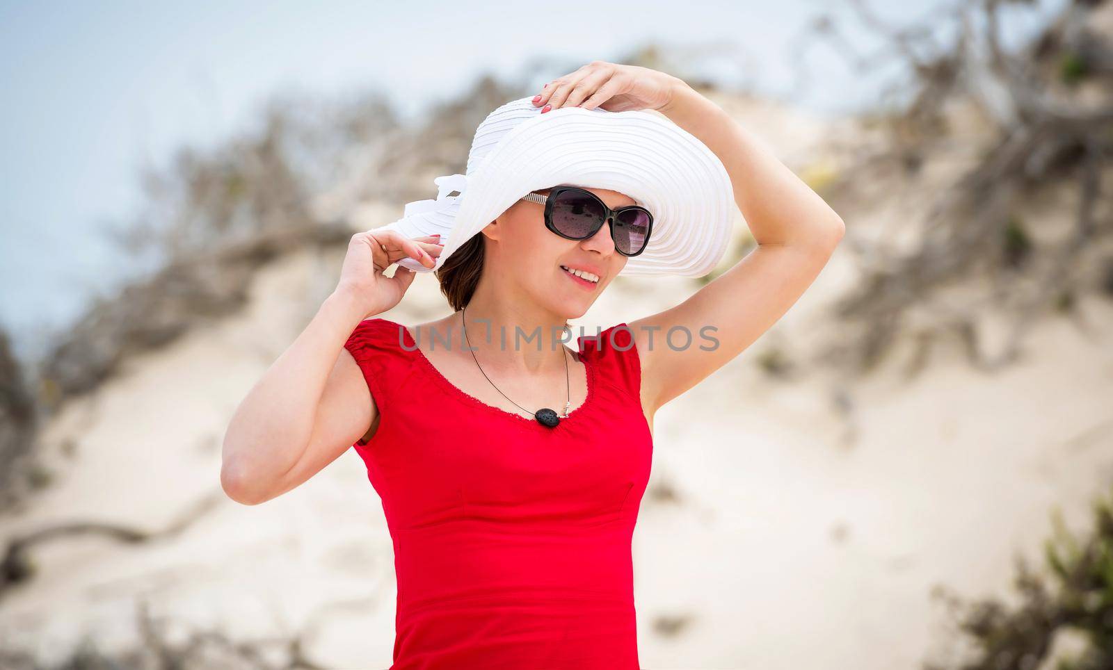 beautiful young woman in evening red dress and white hat on a background of a sand desert