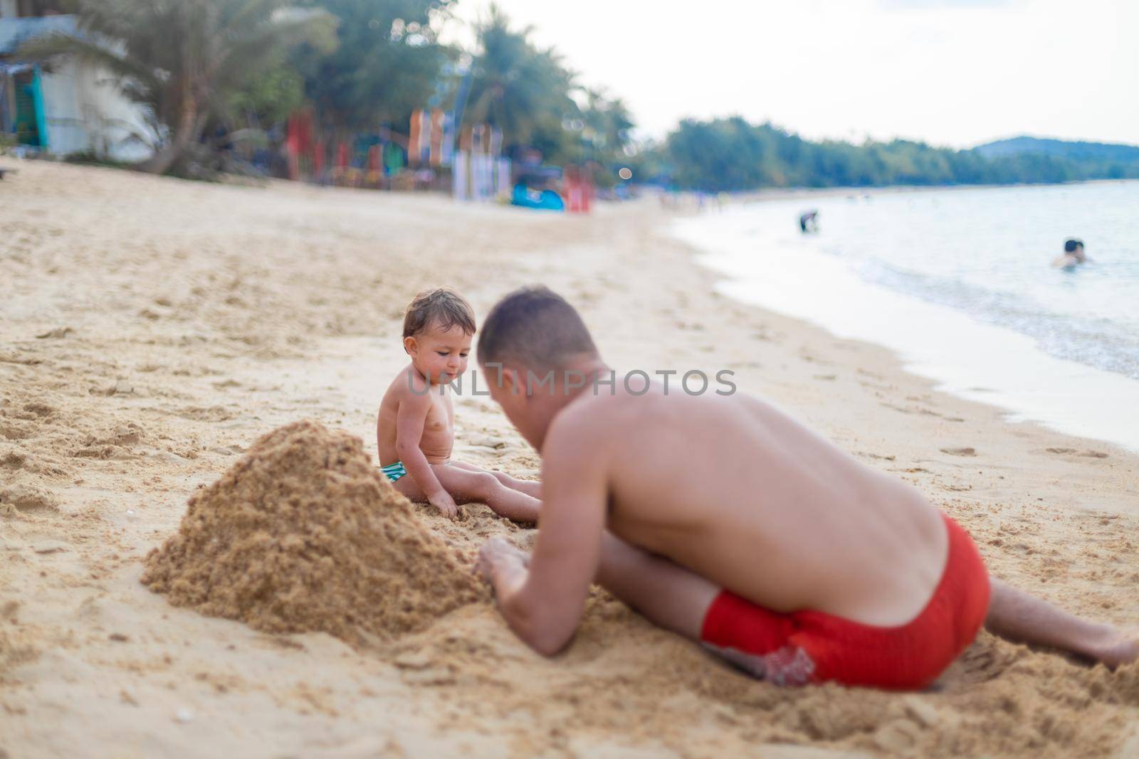 cute toddler kid playing in the sand with father by the sea. by Mariaprovector