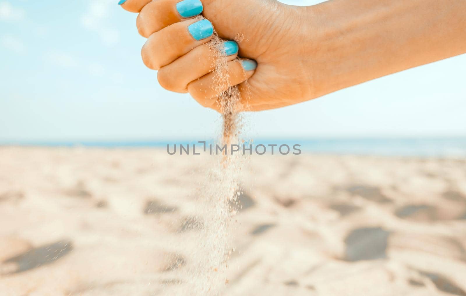 Female hand pours sand on coastline, beach summer vacations.