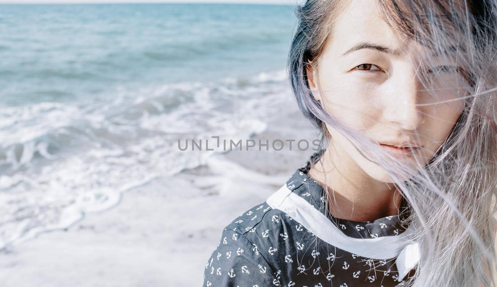 Portrait of young woman on background of sea waves, looking at camera.