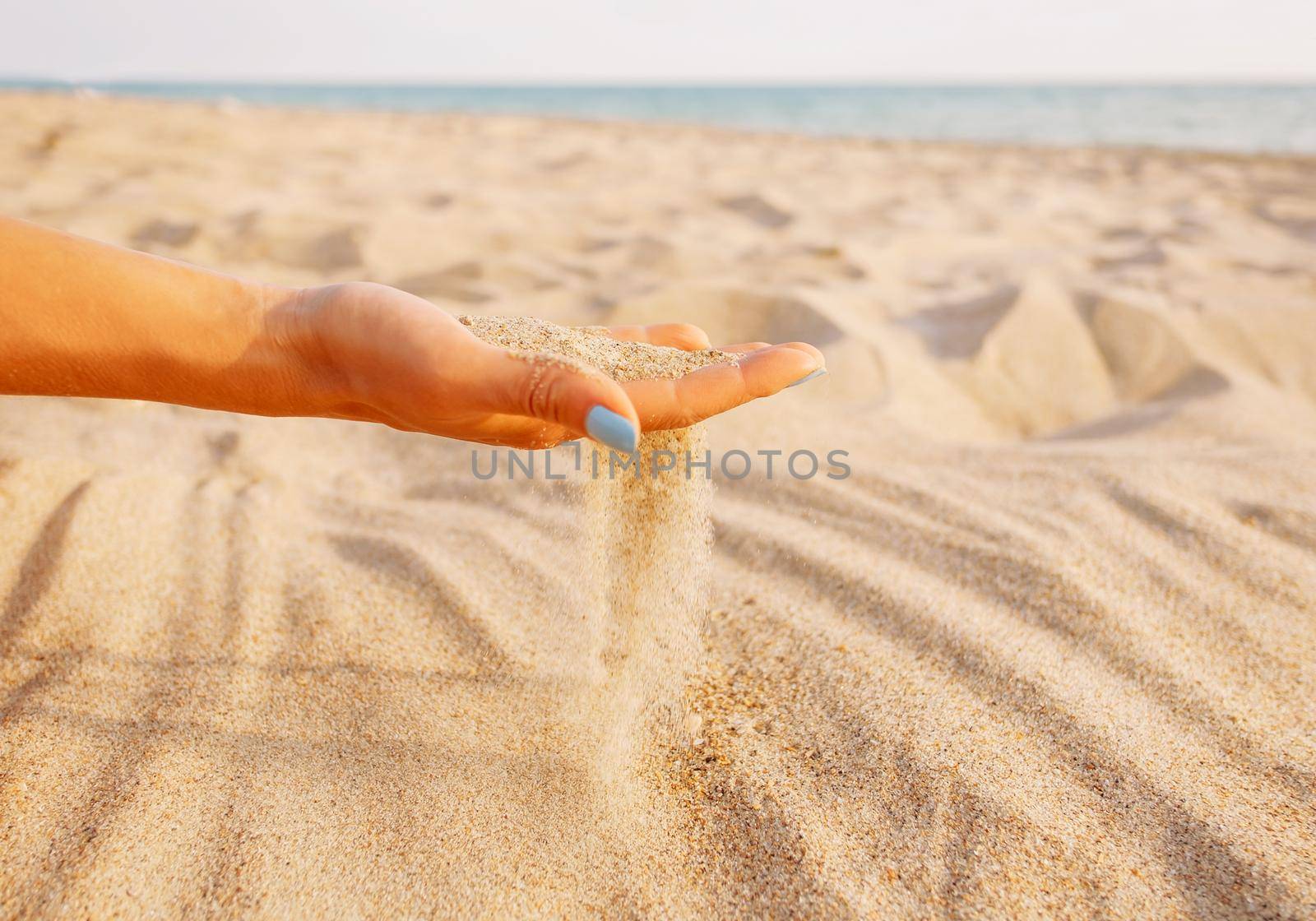 Sand flowing through hand on shore. by alexAleksei