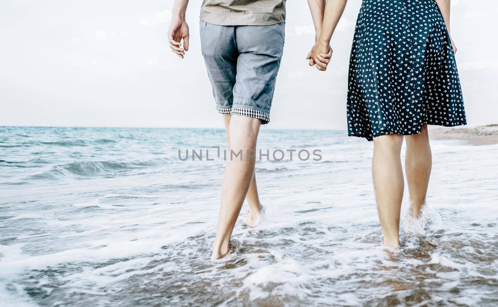 Unrecognizable young loving couple walking on sea coast and holding hands, summer vacations.