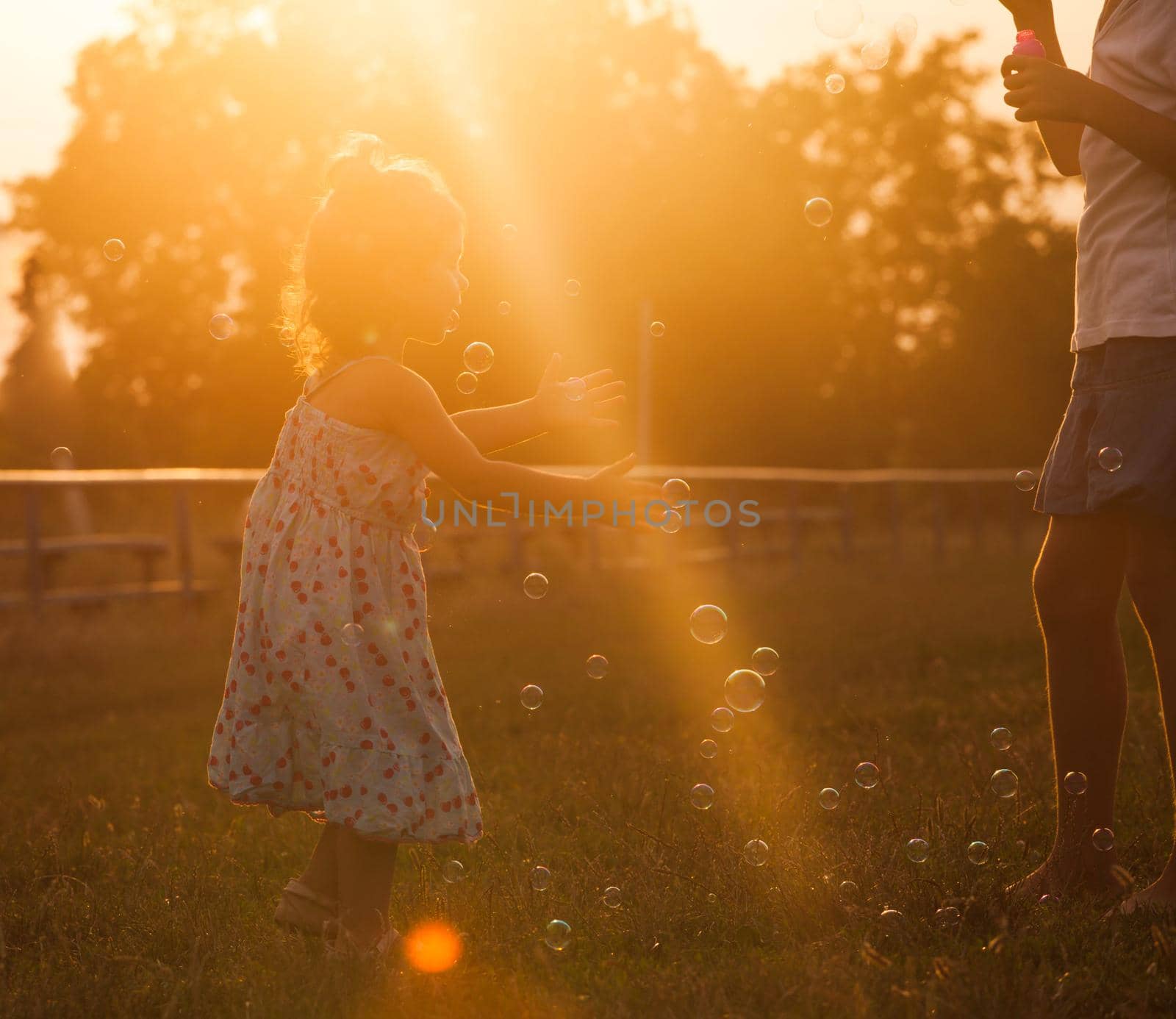 Pretty girl runs for the bubbles in the park on the sunset