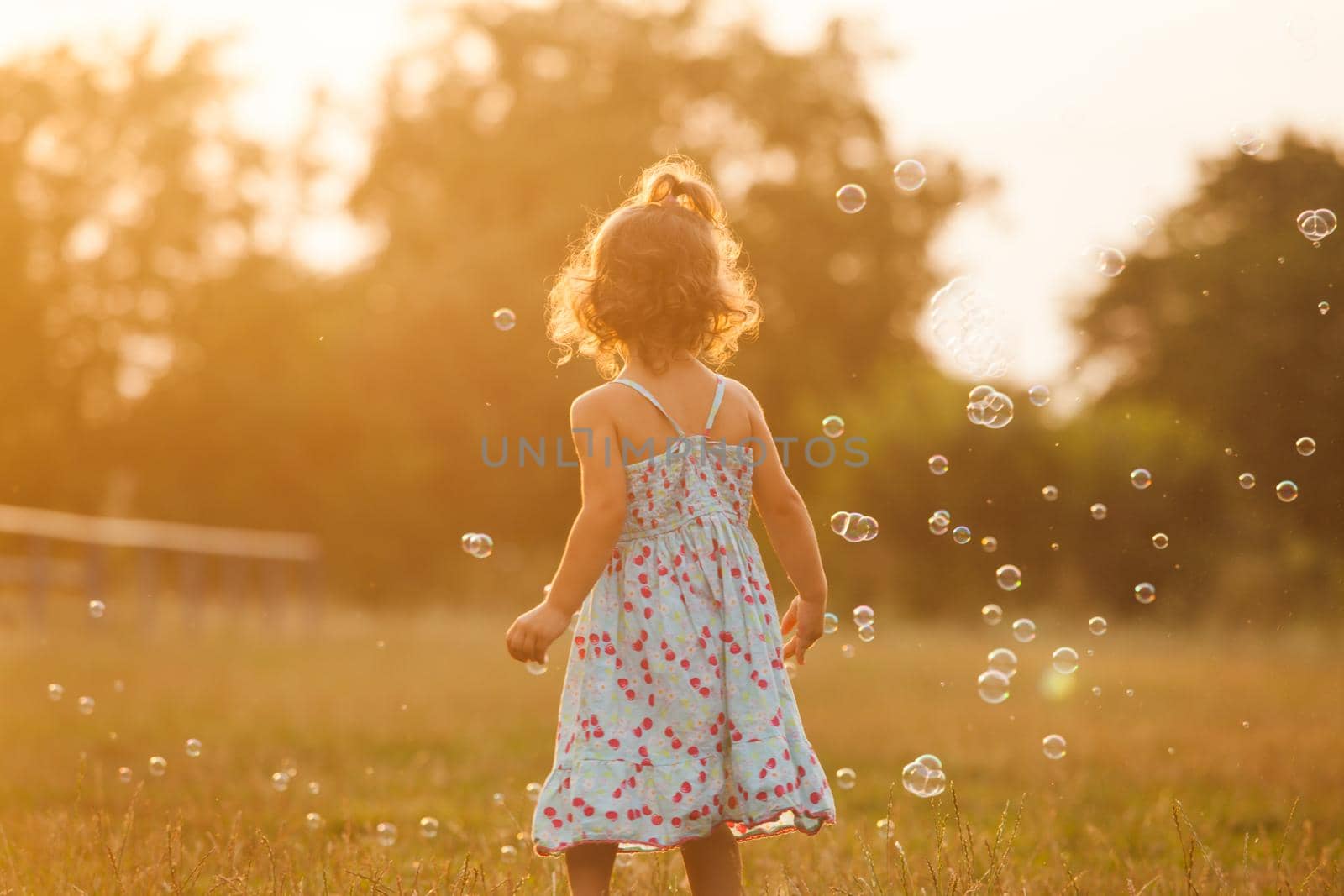 Pretty girl runs for the bubbles in the park on the sunset