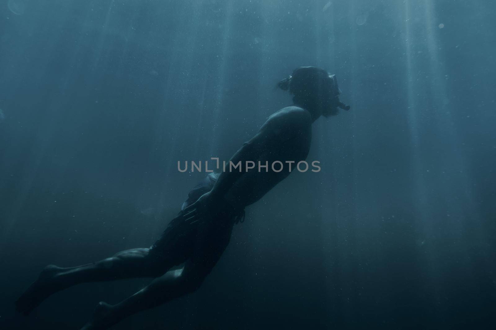 Young man swimming underwater in blue sea among sunbeams, sea vacations.