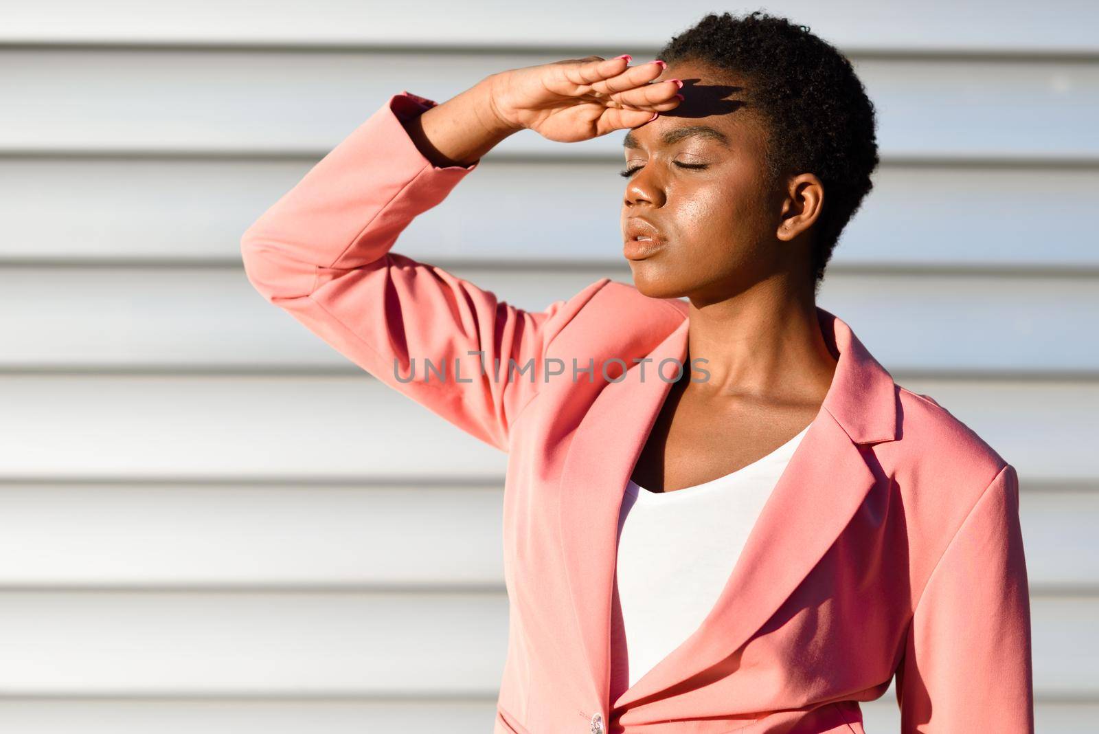 Black woman, model of fashion, standing on urban wall. African american female wearing suit with pink jacket with sunset light.