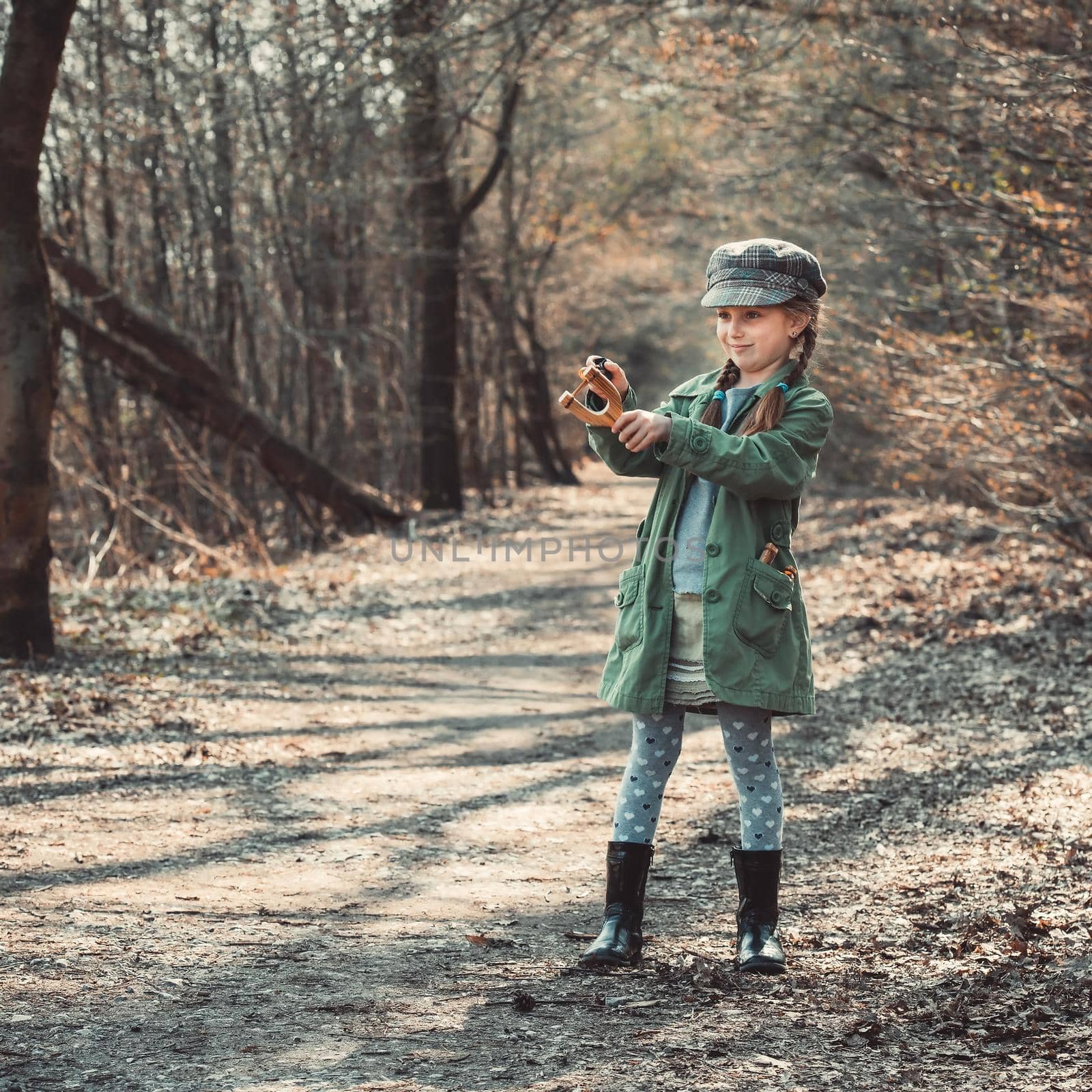 little girl playing with a slingshot in the woods, photo in vintage style