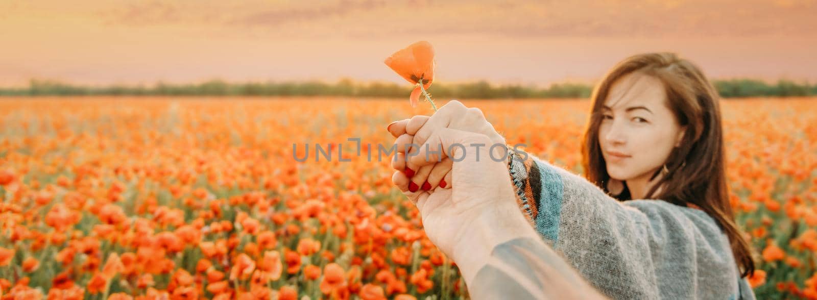 Smiling beautiful young woman leading man in flower summer meadow, point of view shot. Focus on hand.