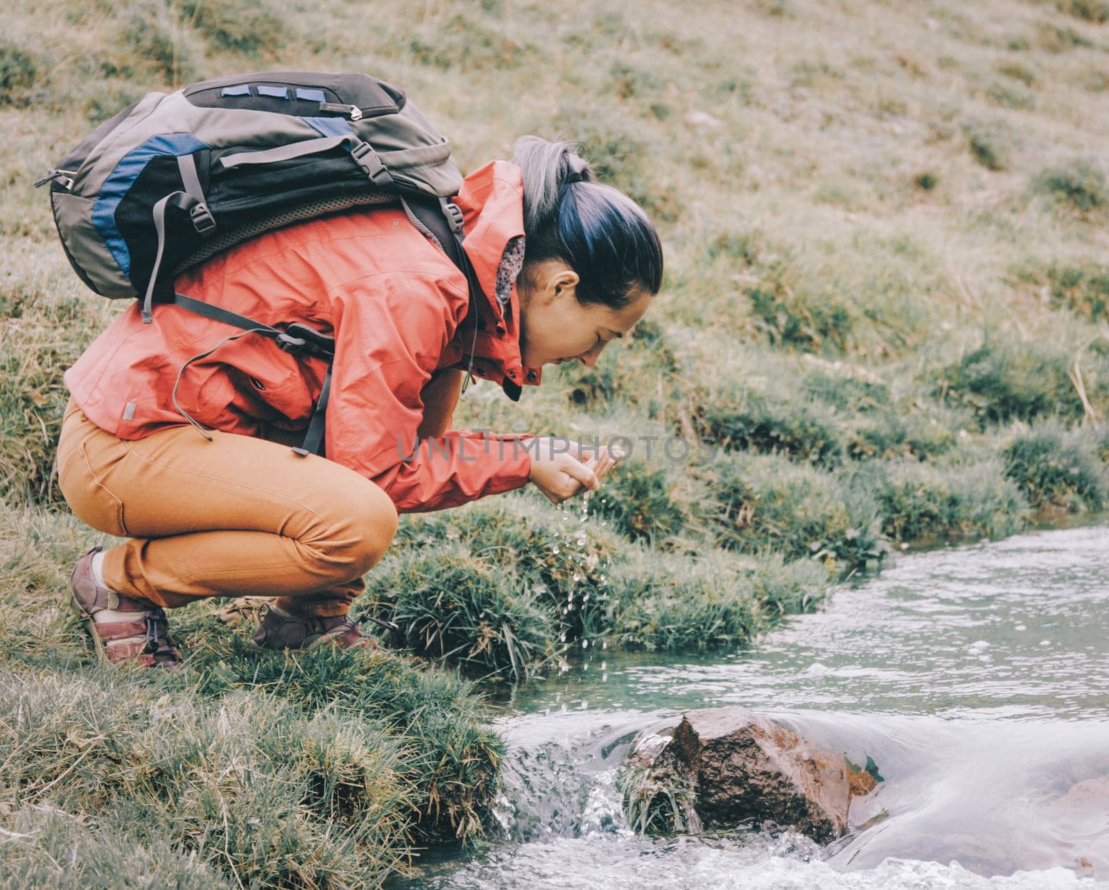 Backpacker woman drinking water from creek with her hands. by alexAleksei