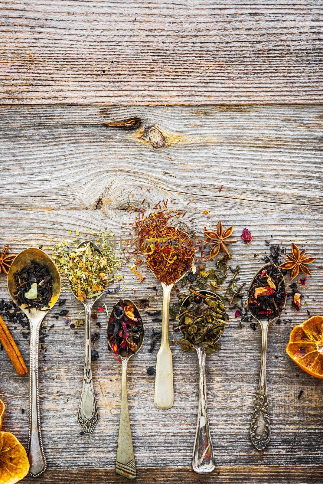 assortment of dry teas in silver spoons on wooden background