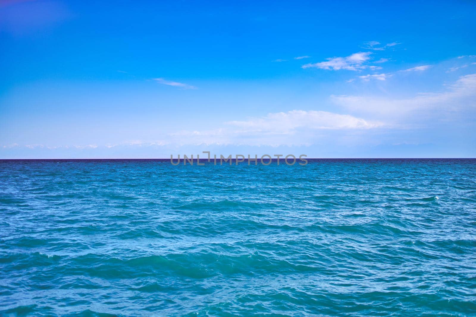 Seascape with clear horizon line and clouds on blue sky. Travel background and banner. Ocean waves.