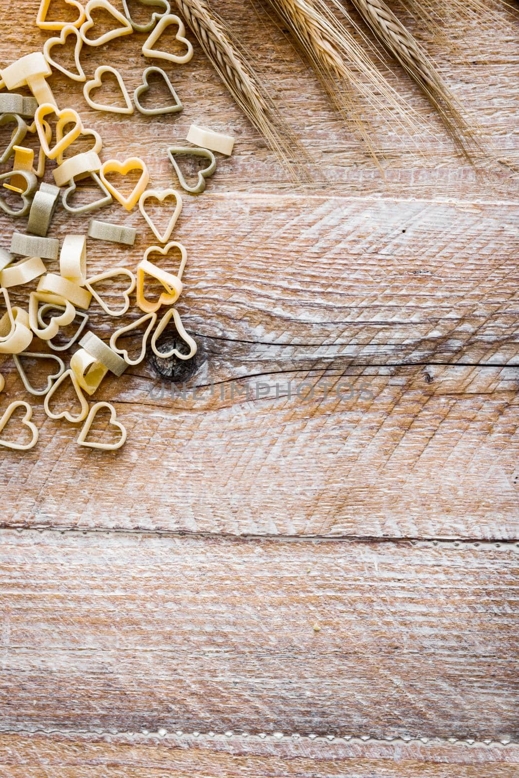 Heart shaped pasta with wheat ears on a wooden textured table