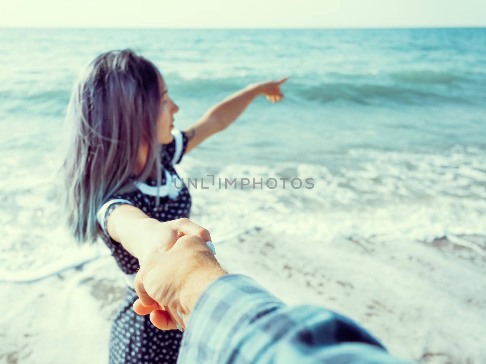 Beautiful young woman holding man's hand and pointing at sea, point of view. Focus on male hand.