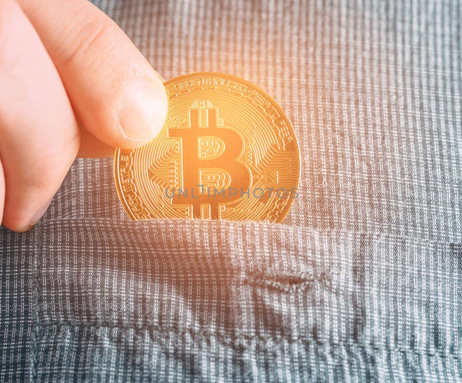 Hand putting glowing gold bitcoin into pocket of shirt, symbol of crypto currency and virtual money, close-up.