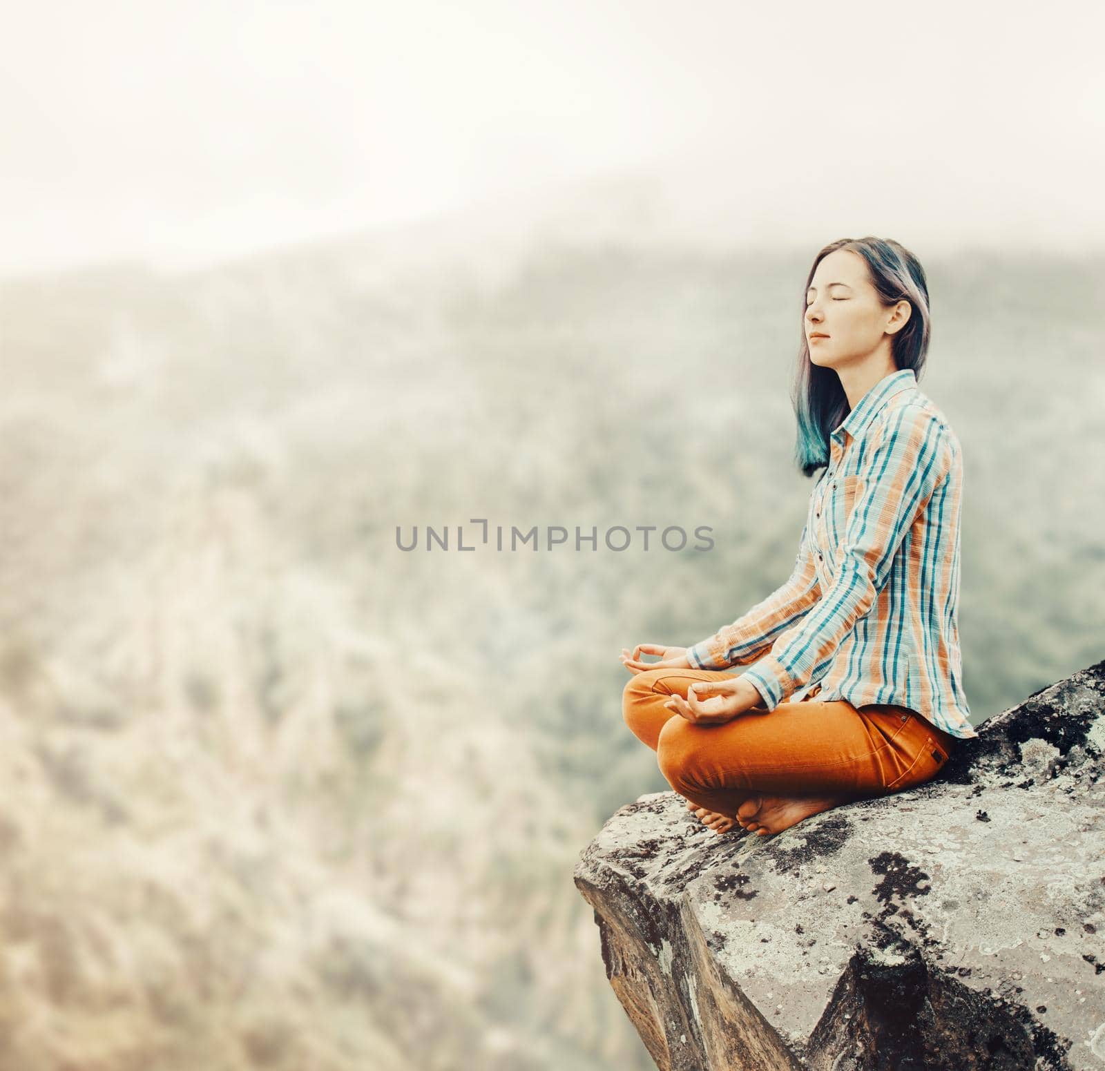 Traveler young woman relaxing on edge of rock in pose of lotus in the mountains outdoor.