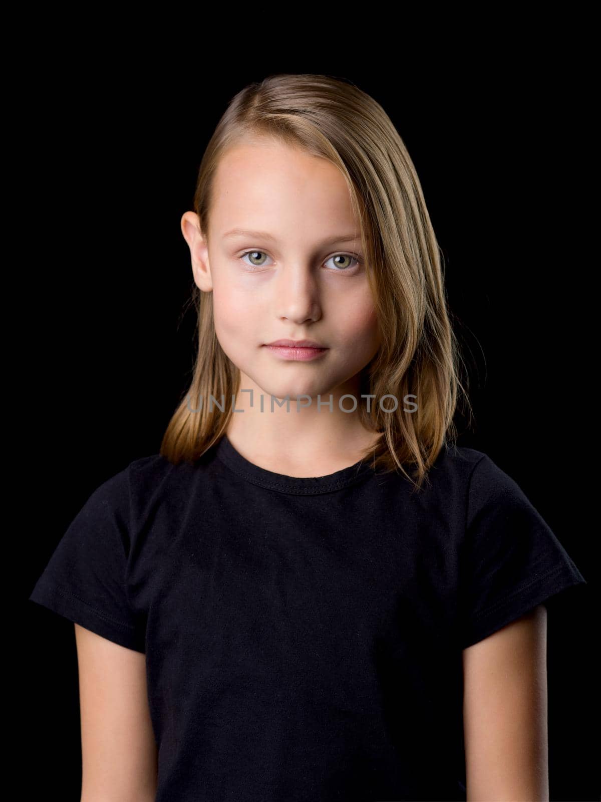 Beautiful girl posing in the studio. Close-up portrait of a beautiful blonde teenage girl in a black t-shirt on a black background.
