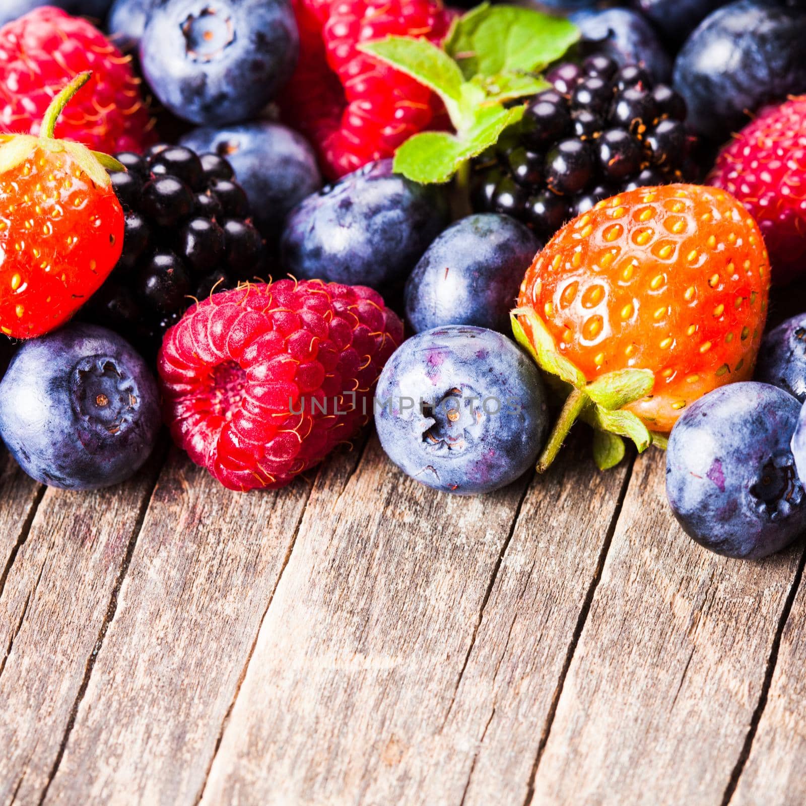 Summer wild berries over shabby wooden background. Raspberry, strawberry, blackberry and blueberry on the table