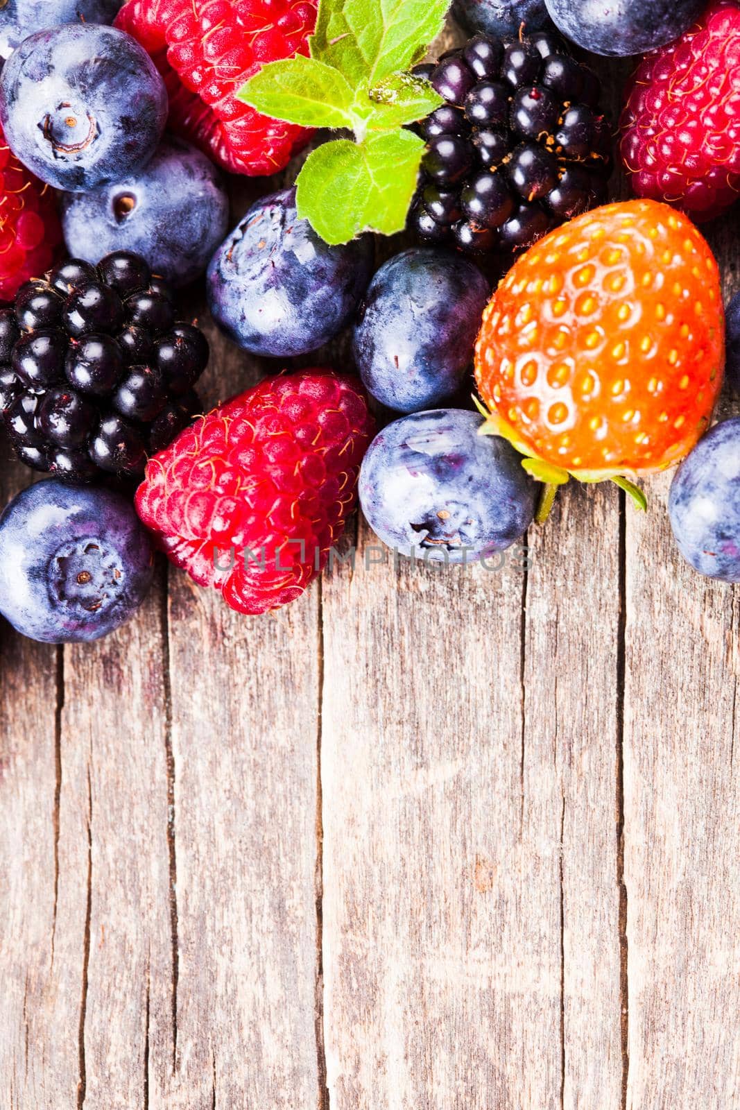 Summer wild berries over shabby wooden background. Raspberry, strawberry, blackberry and blueberry on the table