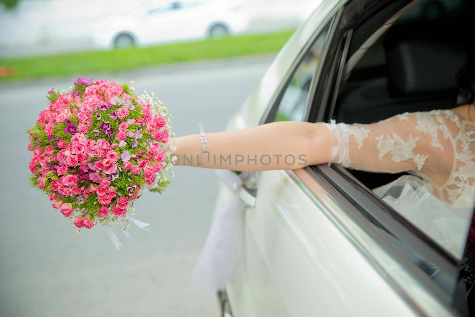 The bride took out the pink flower bouquet out of the car . bride girl goes to wedding cars and waving with a bouquet out of it. The bride's bouquet of flowers. Wedding day. by Adil_Celebiyev_Stok_Photo