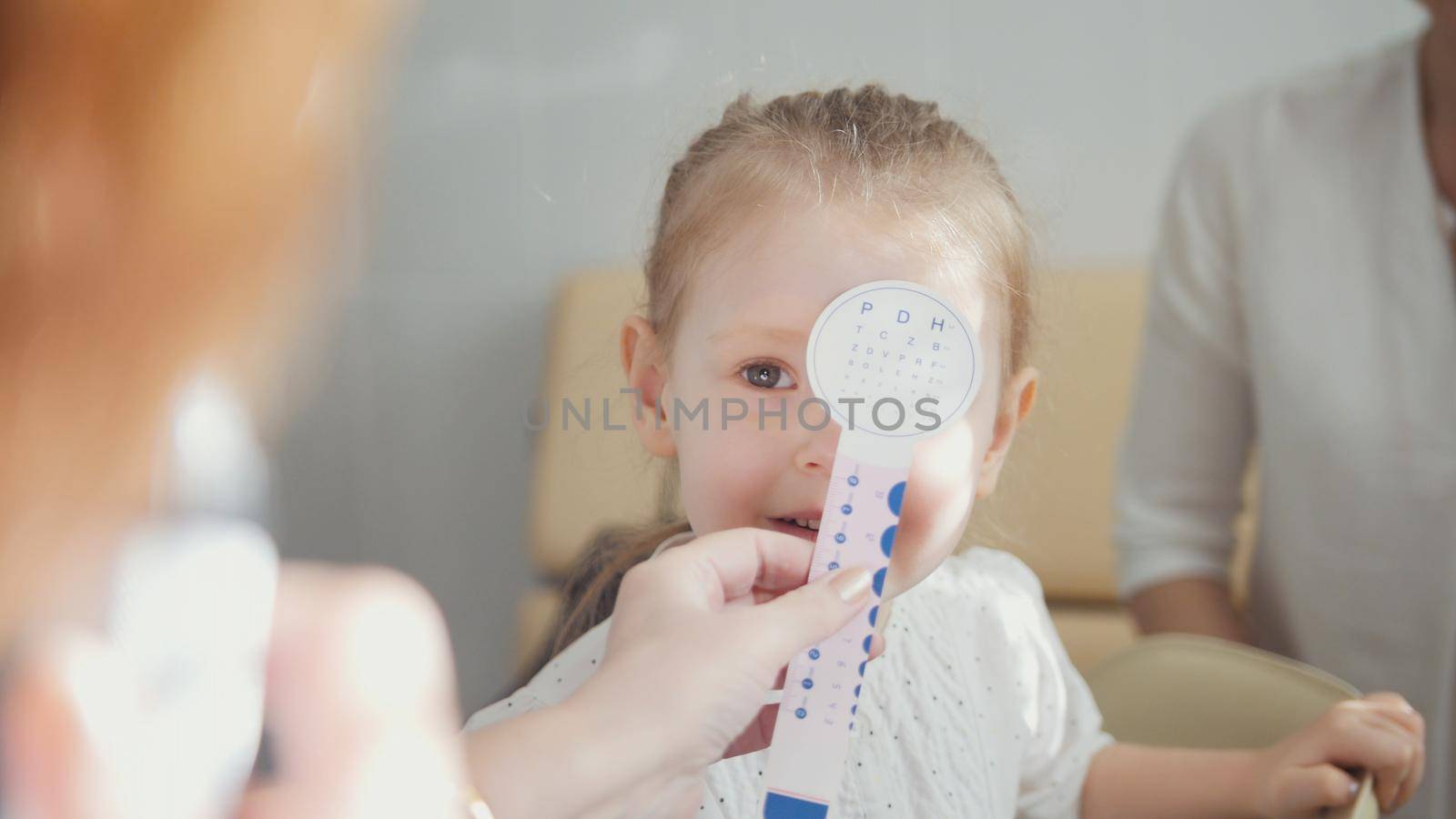 Cute blonde girl with mommy in child's ophthalmology - optometrist diagnosis eyesight, close up