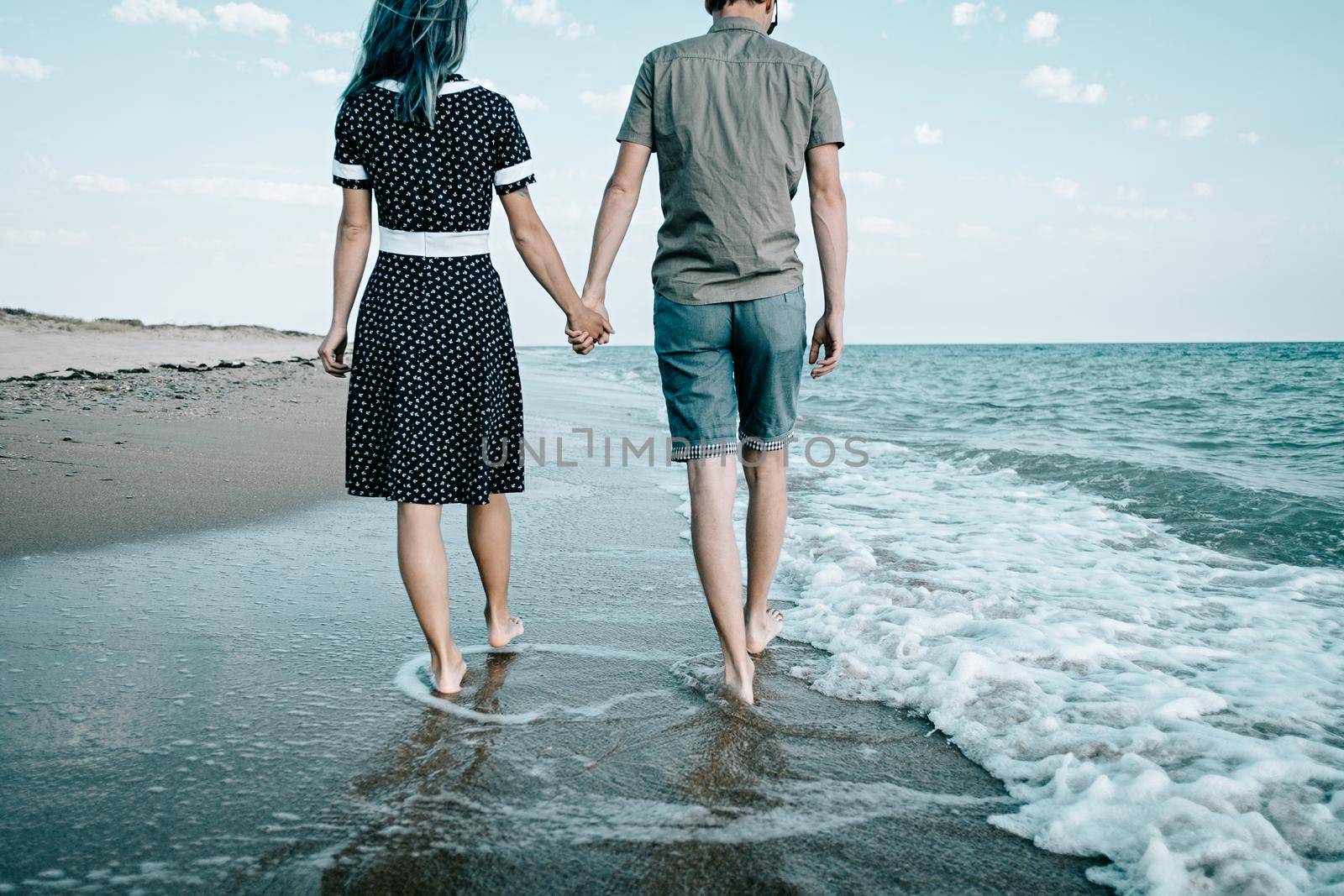 Young loving couple walking on sand coast near the sea and holding hands together, beach summer vacations.