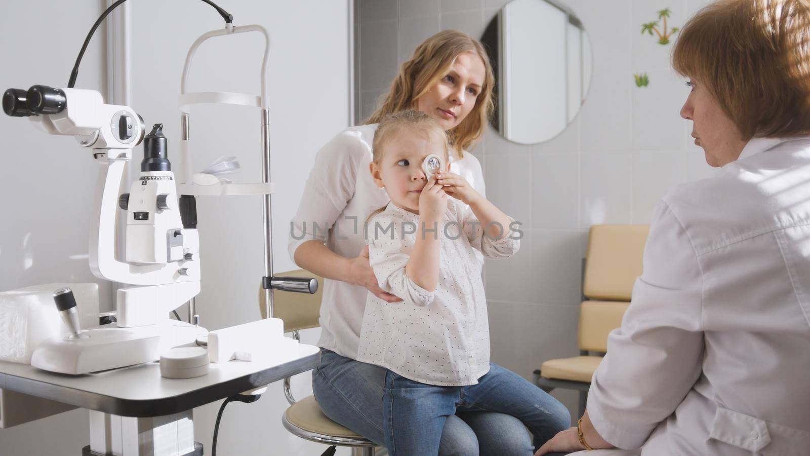 Ophthalmologist in clinic explains diagnosis about girl's eyesight - child plays by Studia72