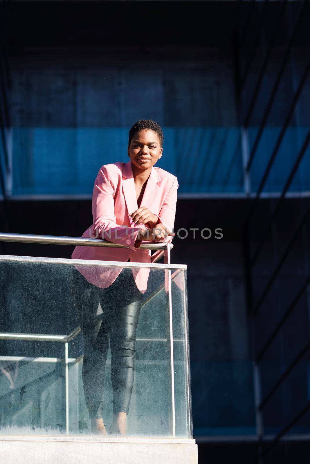 Happy black businesswoman standing near business office building. African american female wearing suit with pink jacket.