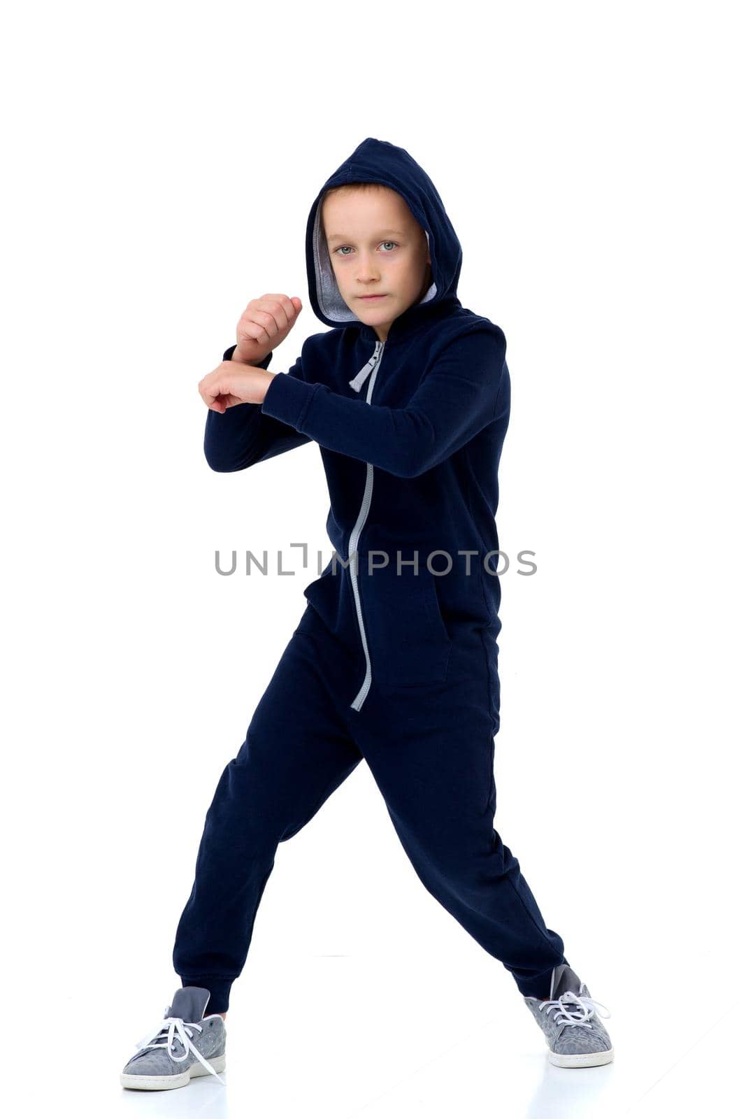 Preteen boy in blue warm overalls. Handsome stylish boy wearing hooded jumpsuit posing against white background in studio
