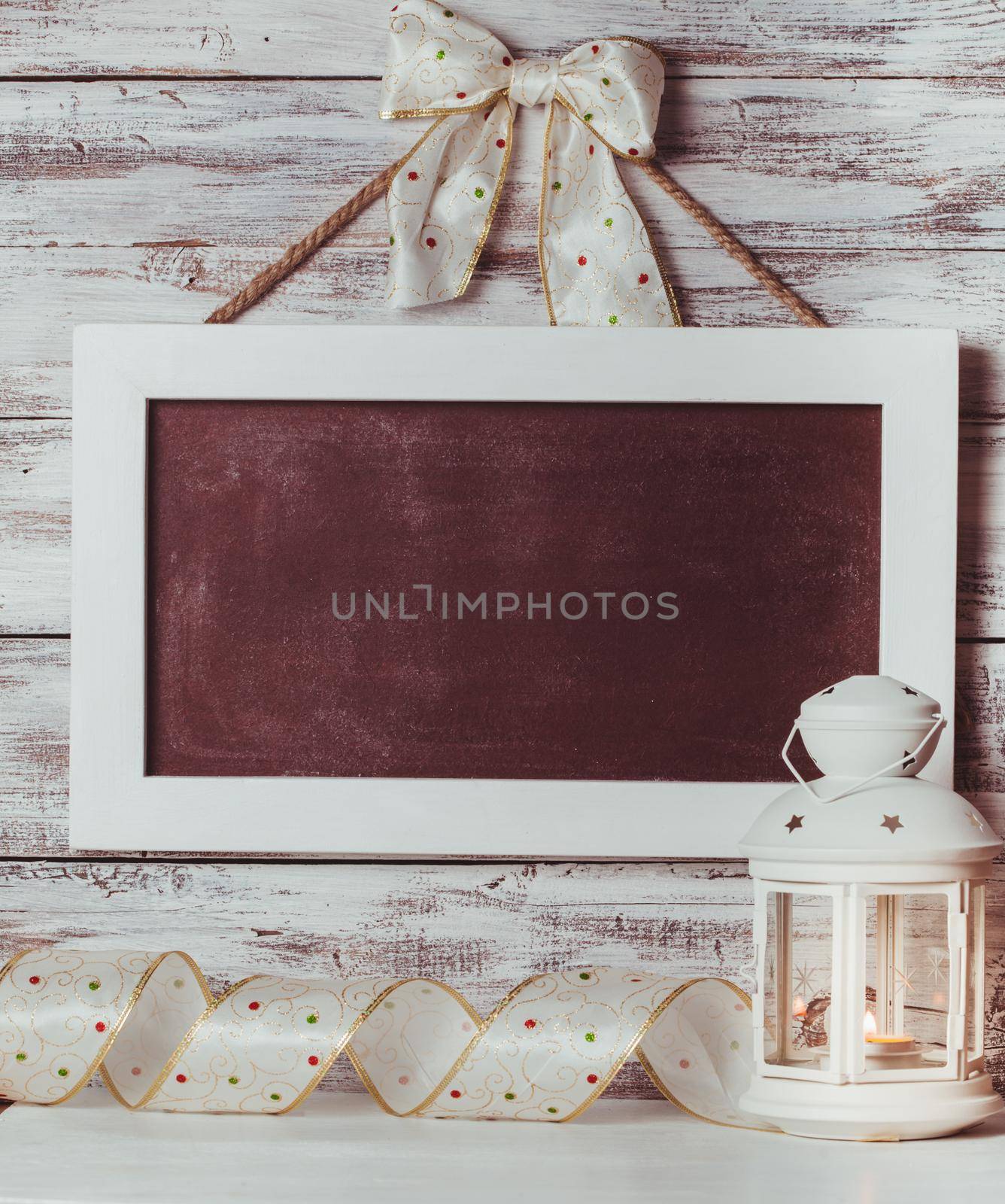 Cristmas lantern with board for greetings over shabby wooden wall and holiday ribbon