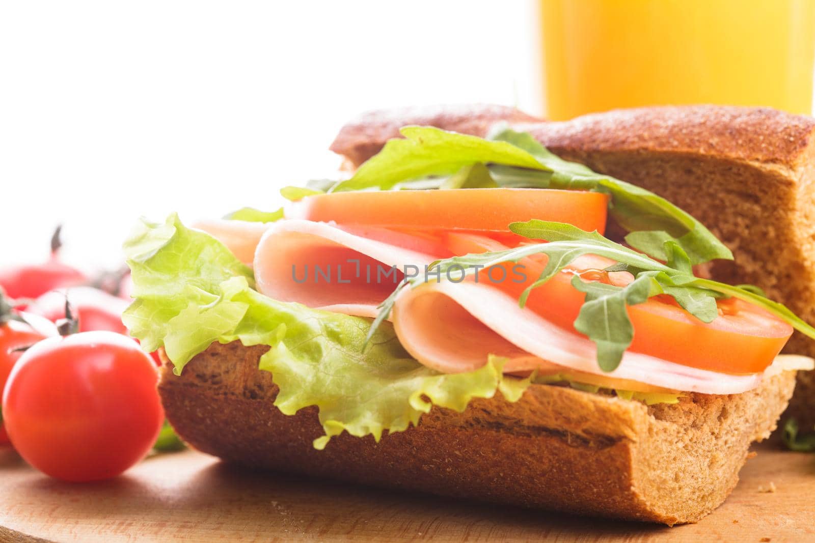 Wholegrain sandwich with ham, tomato, lattuce and arugula with glass of orange juice. Breakfast