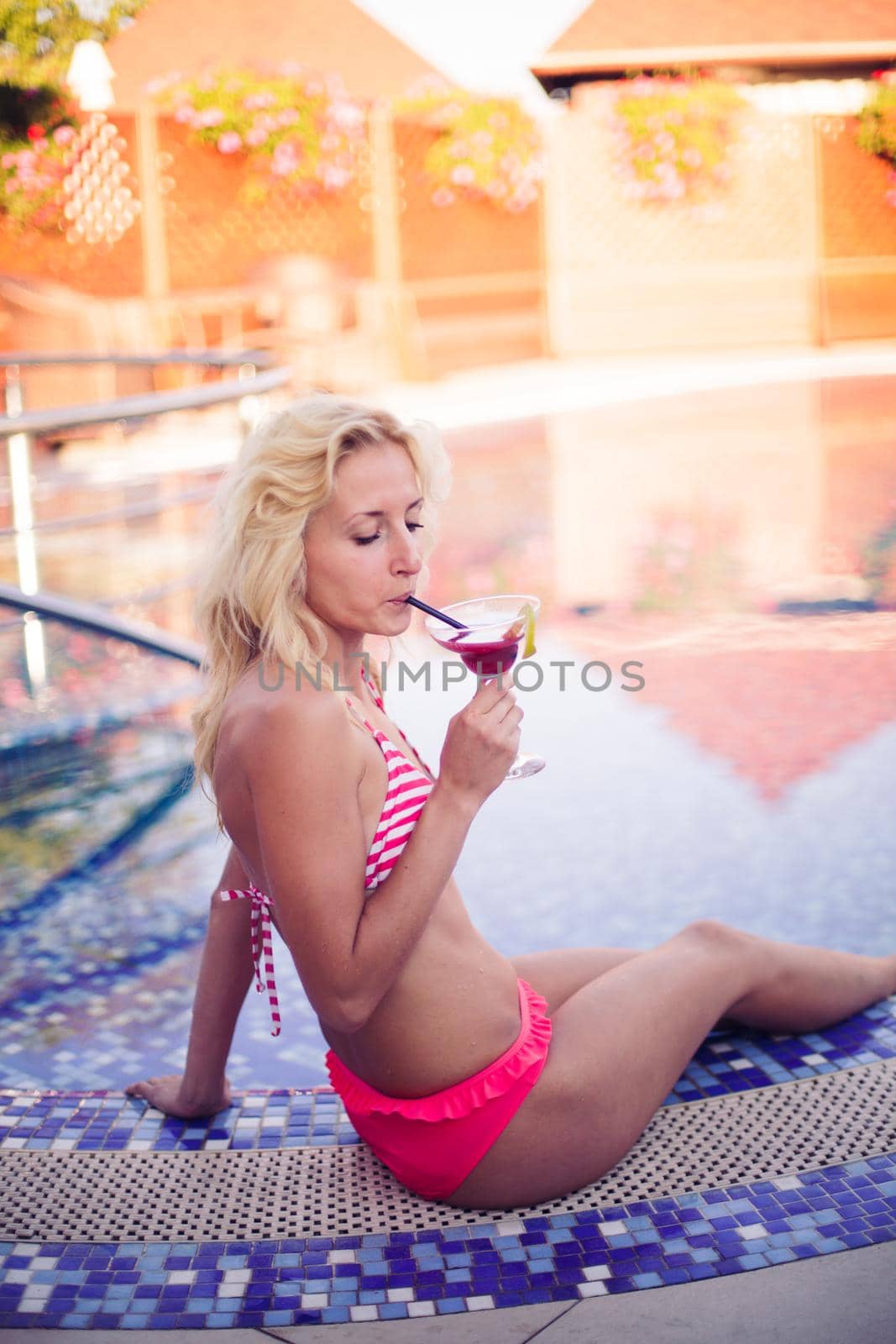 Blonde woman drinks cocktail at the swimming pool
