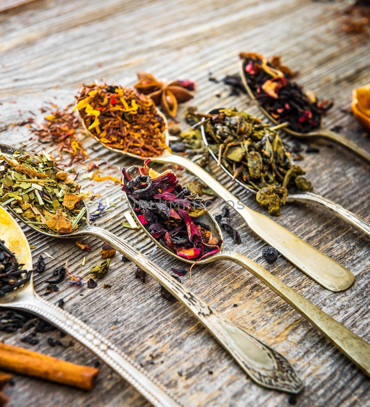 assortment of dry teas in silver spoons on wooden background