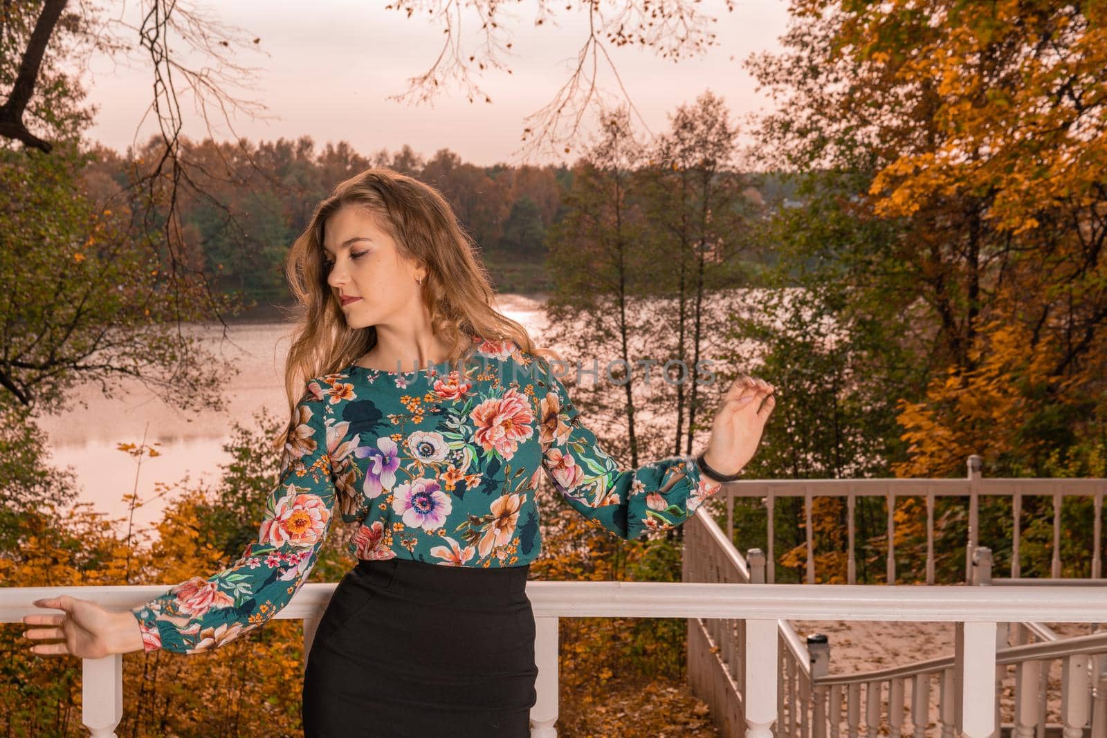 A beautiful woman stands leaning against a white railing, a young blonde with gentle lips, in a colored shirt, stands against a background of steps intellect autumn sensual facial expression bright blue eyes by 89167702191